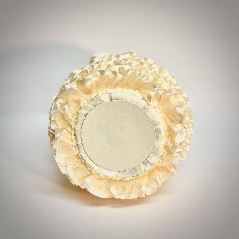 Peut inclure: Un objet d&eacute;coratif rond de couleur cr&egrave;me avec un design superpos&eacute; et &agrave; volants. L'objet a une base circulaire avec un centre de couleur cr&egrave;me plus clair. Les couches &agrave; volants cr&eacute;ent une apparence textur&eacute;e semblable &agrave; une fleur. L'objet est pos&eacute; sur un fond blanc.