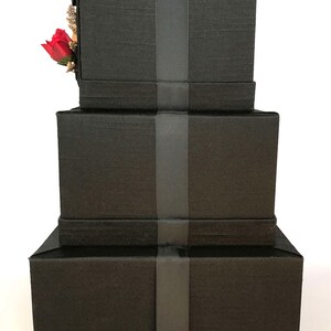 May include: Three black gift boxes stacked on top of each other. Each box has a black ribbon tied around it.