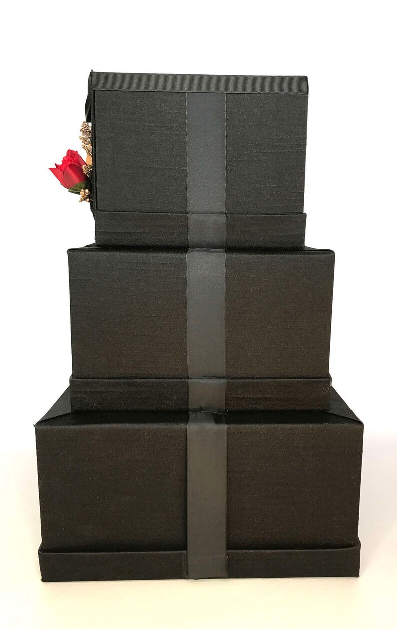 May include: Three black gift boxes stacked on top of each other. Each box has a black ribbon tied around it.