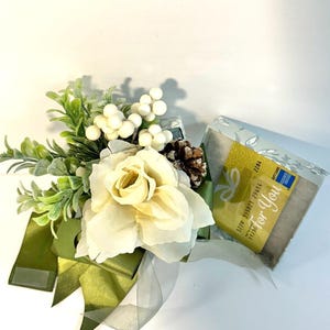 K&ouml;nnte beinhalten: Eine wei&szlig;e Geschenkbox mit gr&uuml;nem Band und einer wei&szlig;en Rose. Die Box ist mit wei&szlig;en Beeren und einer Kiefernzapfen verziert. Die Geschenkkarte in der Box lautet "Just For You".