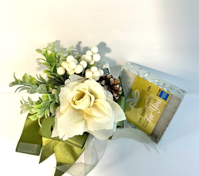 K&ouml;nnte beinhalten: Eine wei&szlig;e Geschenkbox mit gr&uuml;nem Band und einer wei&szlig;en Rose. Die Box ist mit wei&szlig;en Beeren und einer Kiefernzapfen verziert. Die Geschenkkarte in der Box lautet "Just For You".
