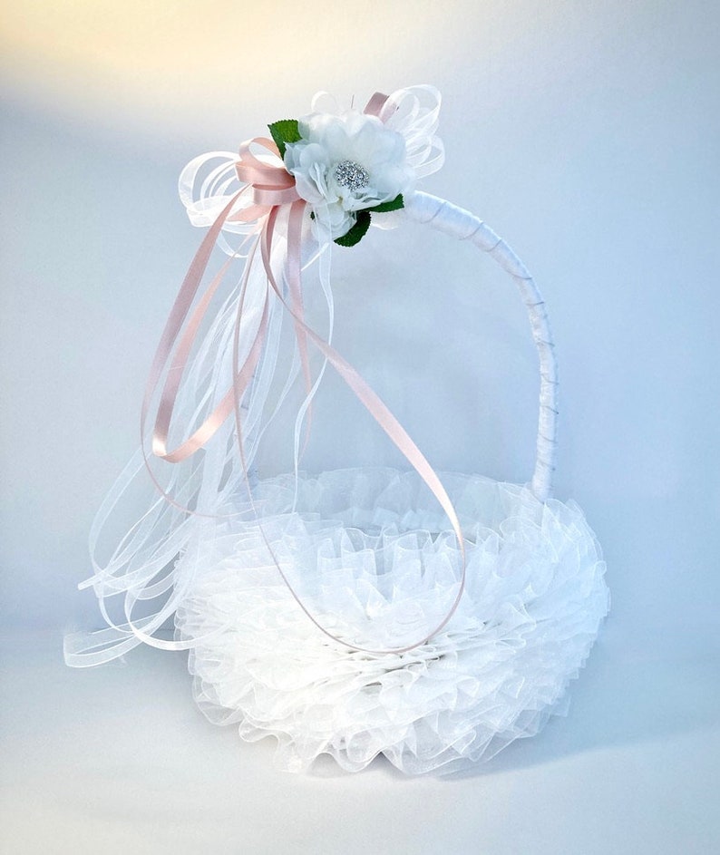 May include: White flower girl basket with a pink satin ribbon and white tulle. The basket is decorated with a white flower and a rhinestone.