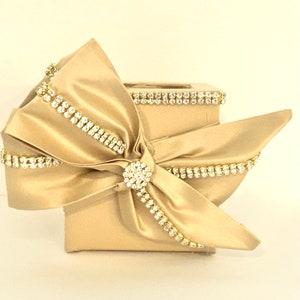 May include: A gold square box with a large satin bow and rhinestones. The bow is tied with a large rhinestone in the center.