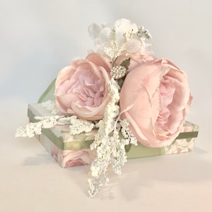 K&ouml;nnte beinhalten: Eine hellgr&uuml;ne Geschenkbox mit Blumenmuster ist mit einem Strau&szlig; rosa Seidenrosen und wei&szlig;en Zweigen verziert. Die Rosen haben eine zarte, gekr&auml;uselte Textur.