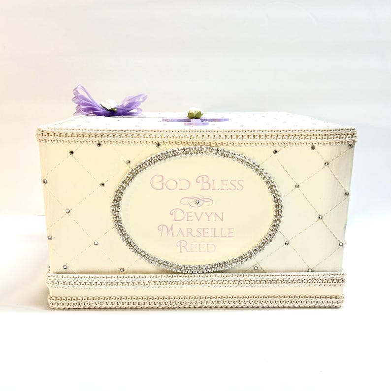 May include: A white gift box with a quilted design and rhinestones. The box has a pink and silver oval label with the text "God Bless Devyn Marseille Reed".