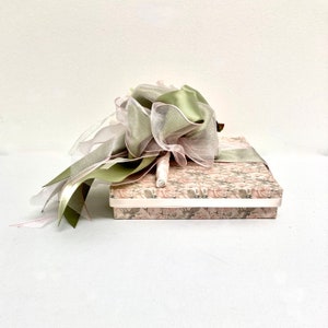 May include: A green and pink floral patterned gift box with a green and pink ribbon and a white tulle bow on top.