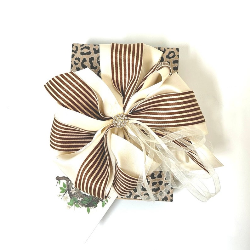 May include: A gift box wrapped in brown and white leopard print paper with a large brown and white striped bow. The bow has a rhinestone embellishment in the center.