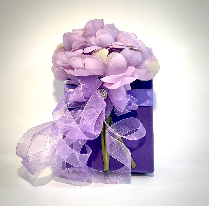 May include: A purple gift box with a bouquet of lavender silk flowers tied with a lavender sheer ribbon and a rhinestone embellishment.