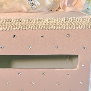 May include: A pink velvet box with a white trim and a clear opening. The box is decorated with rhinestones.