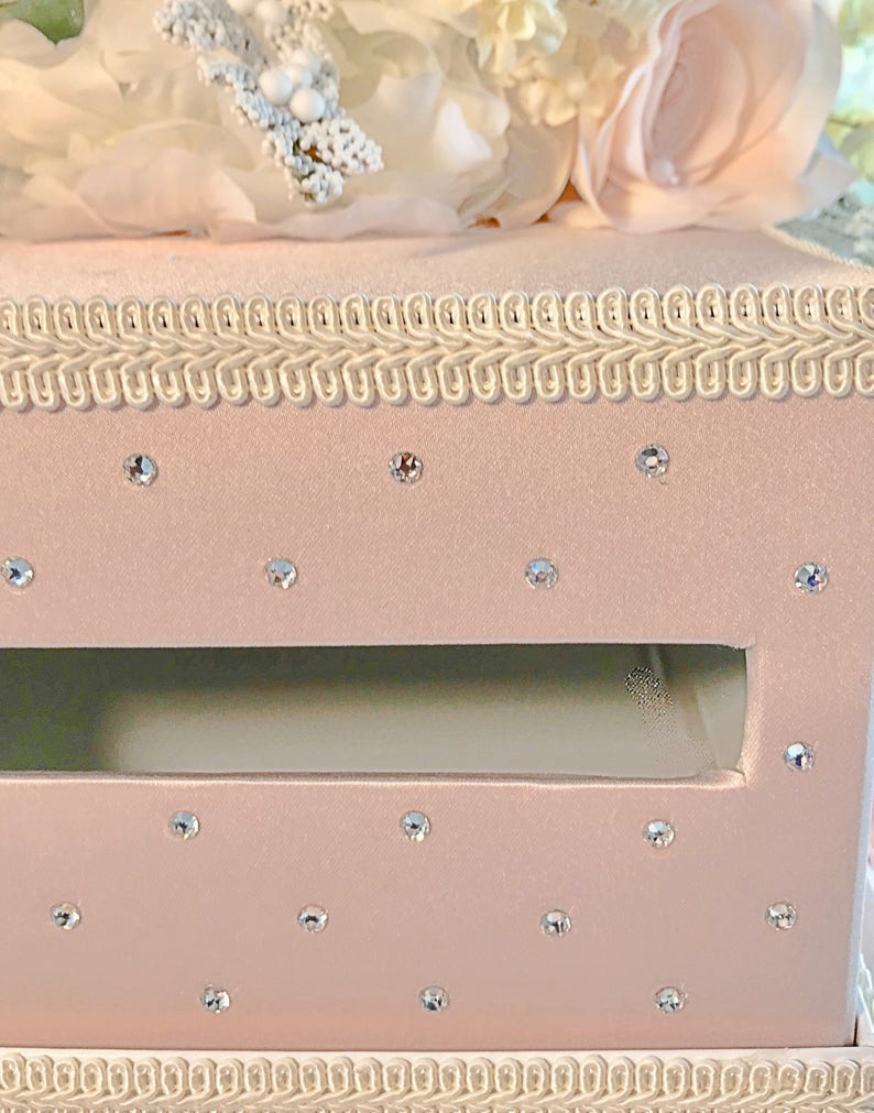 May include: A pink velvet box with a white trim and a clear opening. The box is decorated with rhinestones.