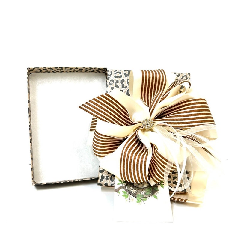 May include: A gift box with a leopard print design and a large brown and white striped bow. The bow has a small rhinestone embellishment in the center.