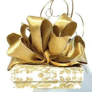 May include: A white gift box with a gold floral pattern and a large gold satin bow.