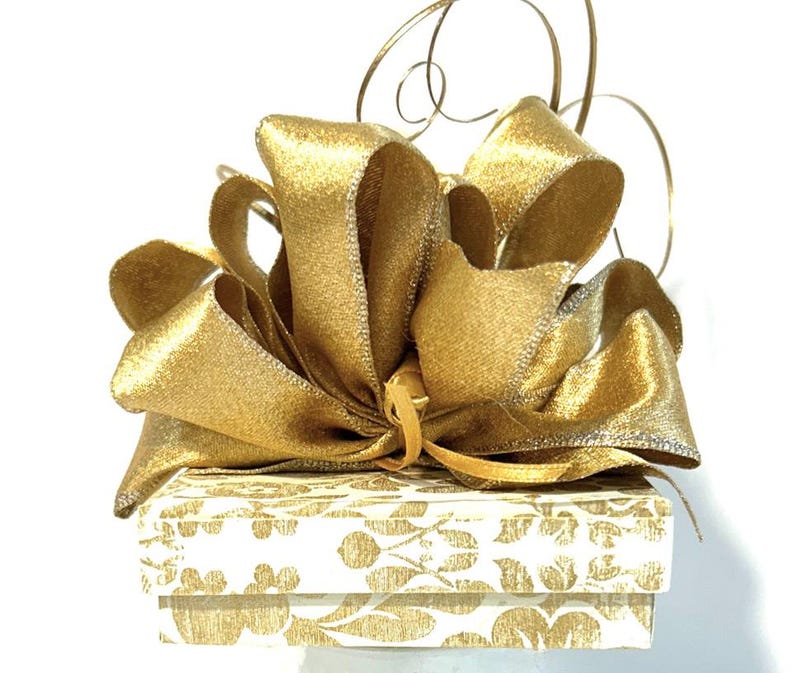 May include: A white gift box with a gold floral pattern and a large gold satin bow.