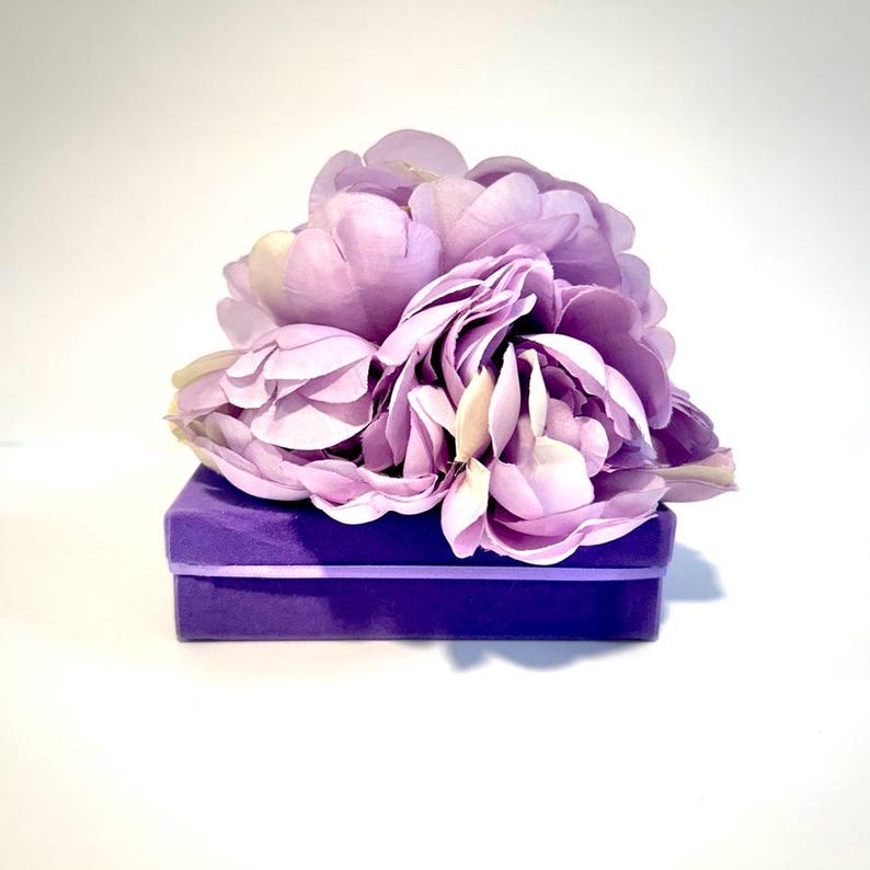 May include: A purple velvet box topped with a cluster of light purple silk flowers.