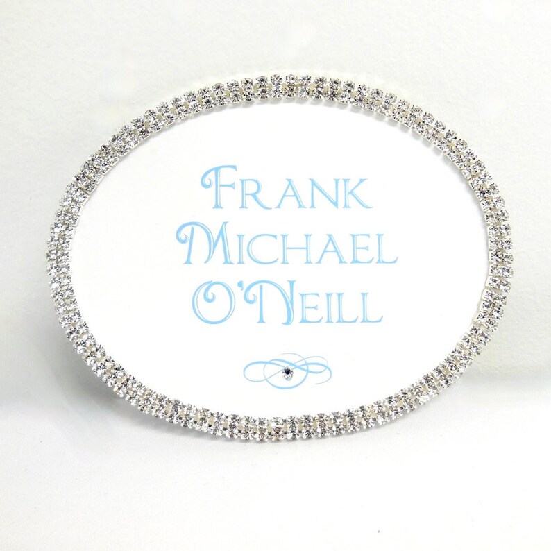 May include: A white oval sign with a silver rhinestone border. The sign says "FRANK MICHAEL O'NEILL" in blue lettering.
