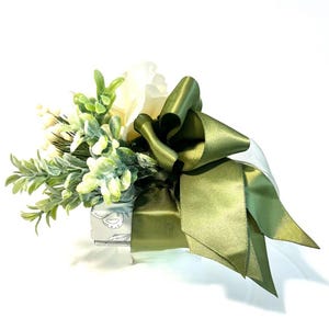 K&ouml;nnte beinhalten: Eine kleine Geschenkbox, die in wei&szlig;es Papier mit gr&uuml;nem Blumendesign eingewickelt ist. Die Box ist mit einem Strau&szlig; wei&szlig;er Blumen und gr&uuml;nem Laub verziert, das mit einer gro&szlig;en gr&uuml;nen Schleife aus Satin gebunden ist.