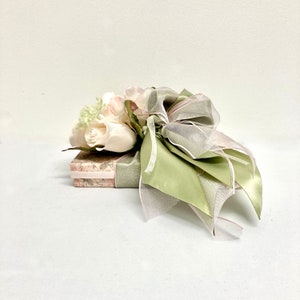 May include: A gift box wrapped in a floral patterned paper with a green and pink ribbon and a bouquet of white roses.
