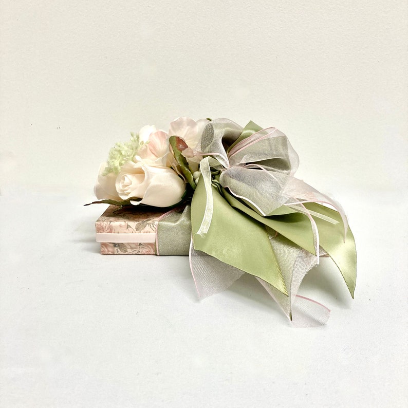 May include: A gift box wrapped in a floral patterned paper with a green and pink ribbon and a bouquet of white roses.