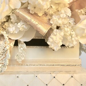 May include: White wedding card box with a white and gold floral arrangement on top. The box has a white satin base with a diamond pattern and rhinestones.