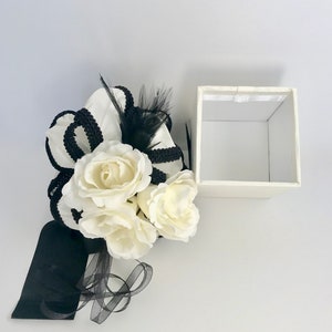 May include: A white gift box with a black ribbon and white flowers. The box is open and empty.