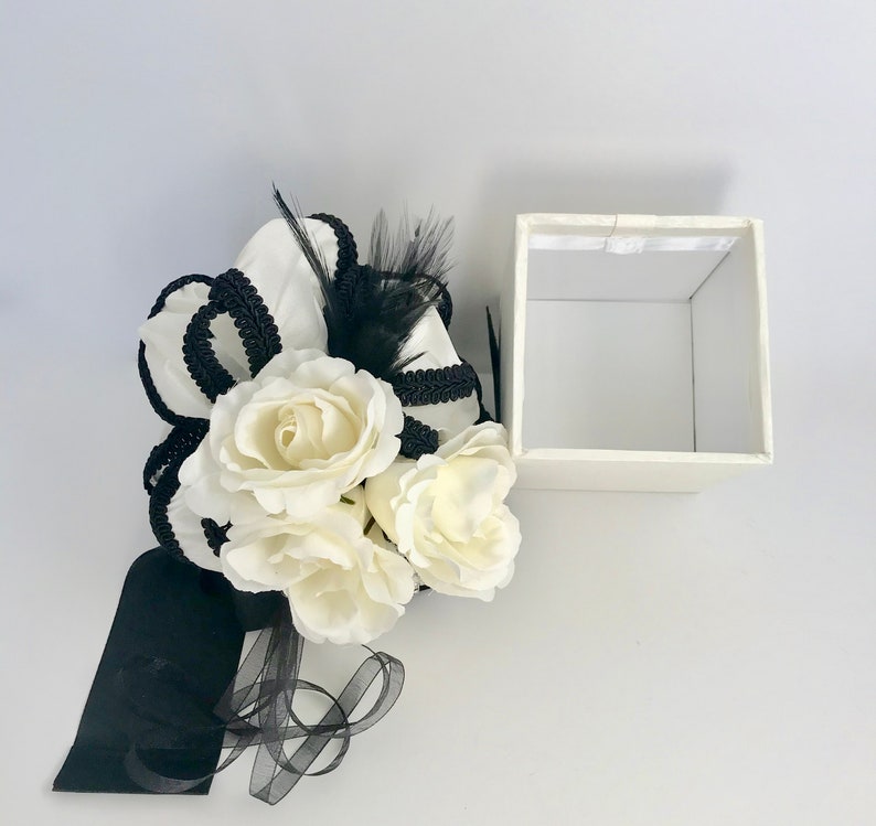 May include: A white gift box with a black ribbon and white flowers. The box is open and empty.