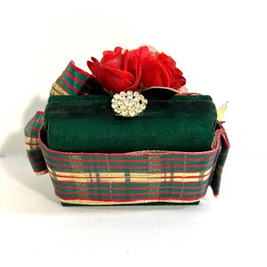May include: A green velvet box with a red and green plaid ribbon and a red flower on top. The box has a clear rhinestone embellishment in the centre.