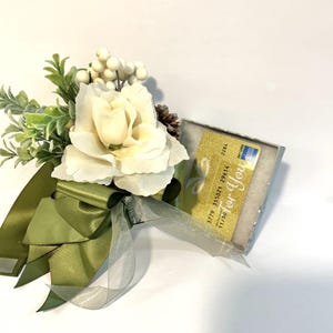 K&ouml;nnte beinhalten: Eine wei&szlig;e Geschenkbox mit einer gr&uuml;nen Schleife und einem wei&szlig;en Blumenarrangement. Die Box enth&auml;lt eine goldene Geschenkkarte mit dem Text "Just for You" und einer Geschenkkarten-Nummer.