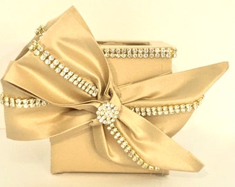 May include: A gold square box with a large satin bow and rhinestones. The bow is tied with a large rhinestone in the center.
