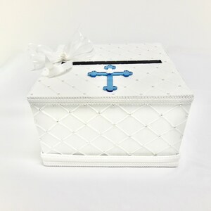 May include: White cardboard box with a blue cross on the lid. The box has a white quilted design and a white satin ribbon.