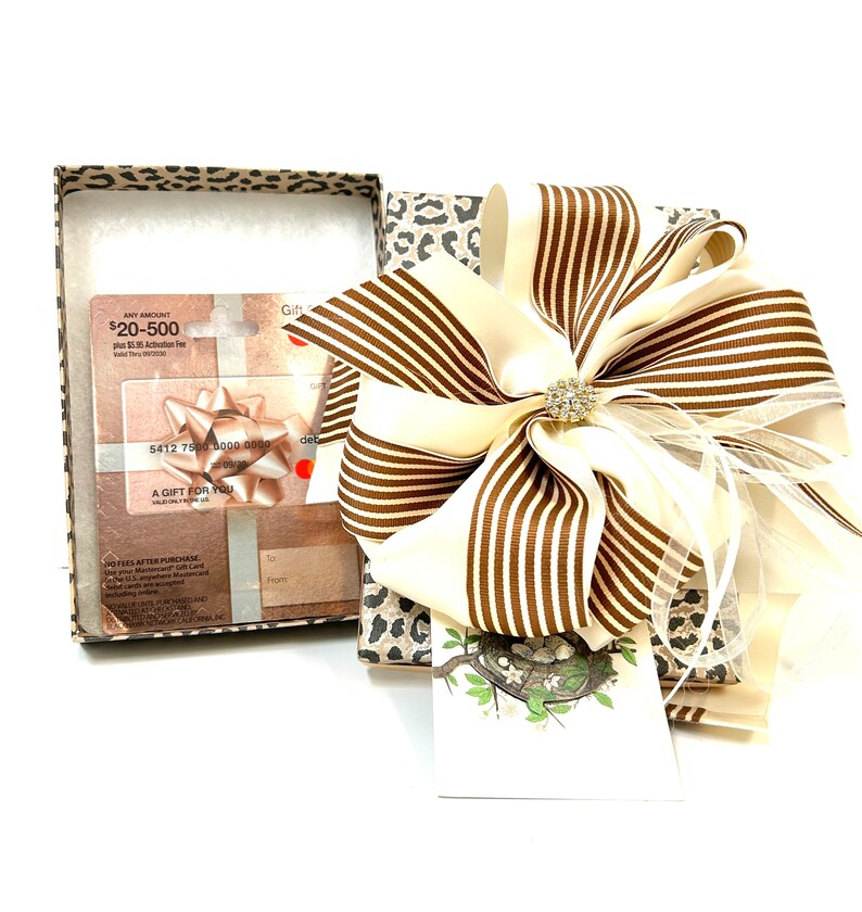 May include: A gift box with a leopard print design, a large brown and white striped bow, and a gift card with the text "ANY AMOUNT $20-500 plus $2.50 Activation Fee" and "A GIFT FOR YOU".