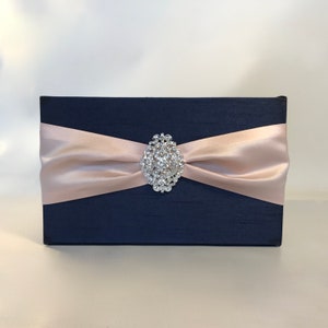 May include: A navy blue wedding card box with a blush pink satin ribbon and a rhinestone brooch.