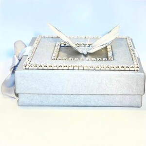 May include: A silver gift box with a white butterfly on top. The box is decorated with a border of rhinestones.