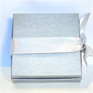 May include: A silver gift box with a white satin ribbon tied around it.