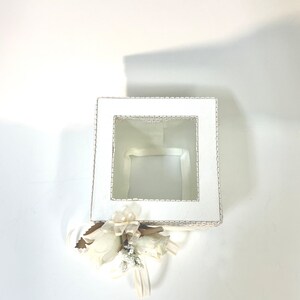 May include: White square tissue box with a lace design and a clear window. The box is decorated with a white flower and ribbon.