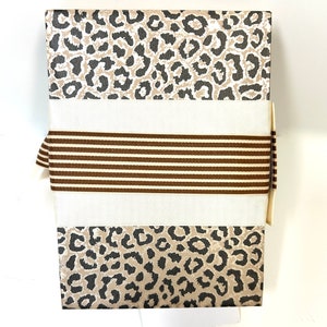 May include: A gift box with a brown and white leopard print design. The box is wrapped with a brown and white striped ribbon.