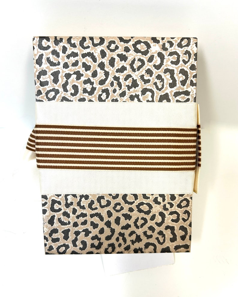 May include: A gift box with a brown and white leopard print design. The box is wrapped with a brown and white striped ribbon.