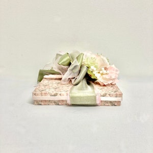 May include: A gift box with a floral design and a green satin ribbon tied with a bow. The box is decorated with pink and white flowers.