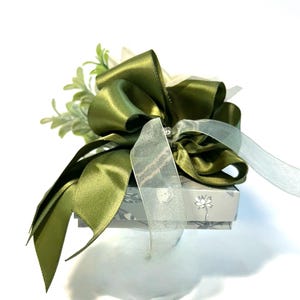 K&ouml;nnte beinhalten: Eine kleine Geschenkbox mit einem gr&uuml;nen Satinband und Schleife. Die Box ist mit einem Blumenmuster verziert und hat einen wei&szlig;en Hintergrund.