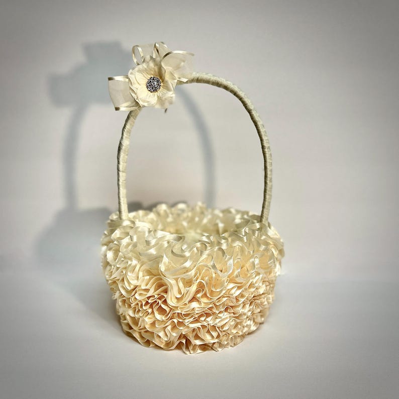 Peut inclure: Panier de demoiselle d'honneur ivoire avec un design &agrave; volants. Le panier est dot&eacute; d'une poign&eacute;e incurv&eacute;e et est orn&eacute; d'un n&oelig;ud et d'une fleur avec un centre en strass. Le panier est fait d'un tissu doux et textur&eacute;.