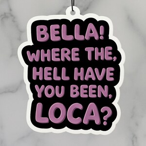 Op de afbeelding: Een witte luchtverfrisser met een zwarte rand en de tekst "BELLA! WHERE THE, HELL HAVE YOU BEEN, LOCA?" in paars. De luchtverfrisser hangt aan een zwart touwtje.