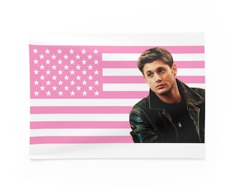 May include: A rectangular wall tapestry featuring a pink American flag design with a portrait of a man wearing a black leather jacket. The flag has pink stripes and white stars.