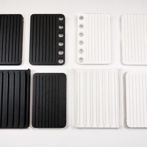 May include: A collection of eight rectangular organisers in black and white. Four organisers feature six circular holes along one side and vertical grooves. Four organisers have a flat surface with vertical grooves, with two featuring raised side edges.