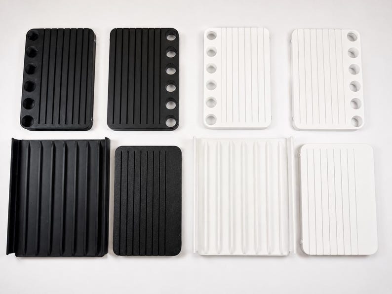 May include: A collection of eight rectangular organisers in black and white. Four organisers feature six circular holes along one side and vertical grooves. Four organisers have a flat surface with vertical grooves, with two featuring raised side edges.