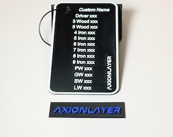 May include: A black golf club tag with white trim and a list of club names and numbers, including "Driver," "3 Wood," and "9 Iron." The text "Custom Name" is at the top. A separate black tag with the blue text "AXIONLAYER" is below.