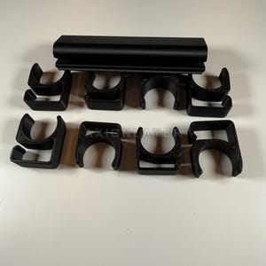May include: A set of eight black plastic C-shaped clips arranged in two rows, with a long black rectangular bar positioned horizontally above them. The text AXIONLAYER is embossed on the surface of the clips, featuring a textured finish.
