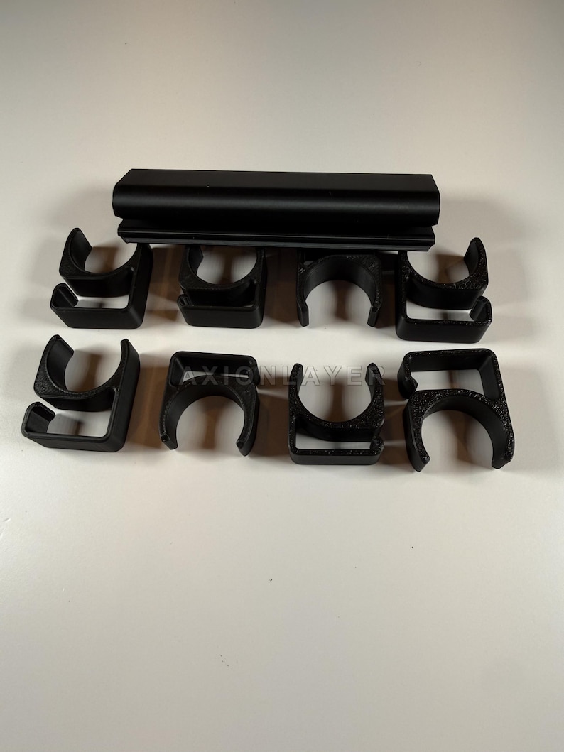 May include: A set of eight black plastic C-shaped clips arranged in two rows, with a long black rectangular bar positioned horizontally above them. The text AXIONLAYER is embossed on the surface of the clips, featuring a textured finish.