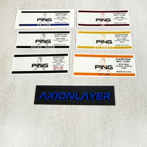 May include: A collection of rectangular labels with the "PING" logo and text, including "ZZ LITE", "MICRO TAPER", "KT-SHAFT", "HEEL-TOE BALANCE", and "KT-M". The labels are white with various colored accents. A black and blue "AXIONLAYER" label is also present.