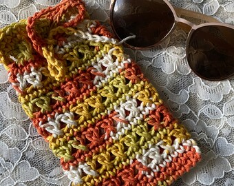 May include: A crocheted sunglasses case with a striped pattern in orange, yellow, and white. The case is made with a textured yarn and has a drawstring closure.