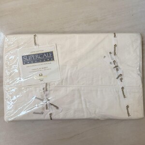 May include: A folded, white twin flat sheet, still in its original packaging. The sheet is labeled "Supercale Easy Care" and made of 100% cotton. The packaging is sealed with a ribbon that says "Wamsutta".