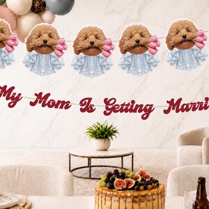 May include: A decorative banner featuring a repeating cutout of a brown poodle wearing a light blue lace collar and holding pink tulips, paired with a separate red script banner that reads My Mom Is Getting Married, strung on white string.
